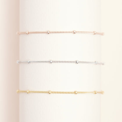 a rose gold bead chain bracelet, a silver bead chain bracelet and a gold bead chain bracelet stack together around a white pole